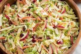 Homemade apple slaw with shredded cabbage, apples, carrots, almonds and dressing shown in a wooden salad bowl.