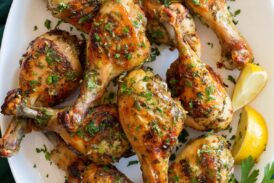Baked chicken legs on a white oval platter with parsley and lemon wedges to the side.