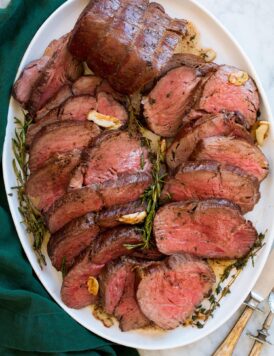 Beef Tenderloin arranged on a white oval platter shown from above on a white marble surface with a green cloth.
