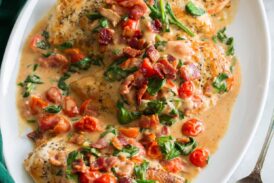 Creamy bacon tomato spinach chicken served on a white oval platter with a green cloth to the side.