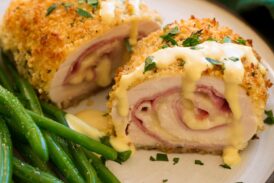 Chicken Cordon Bleu shown sliced in half with sauce on top. Green beans shown to the side.