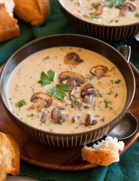 Single serving of cream of mushroom soup in a brown bowl garnished with sauteed mushrooms.