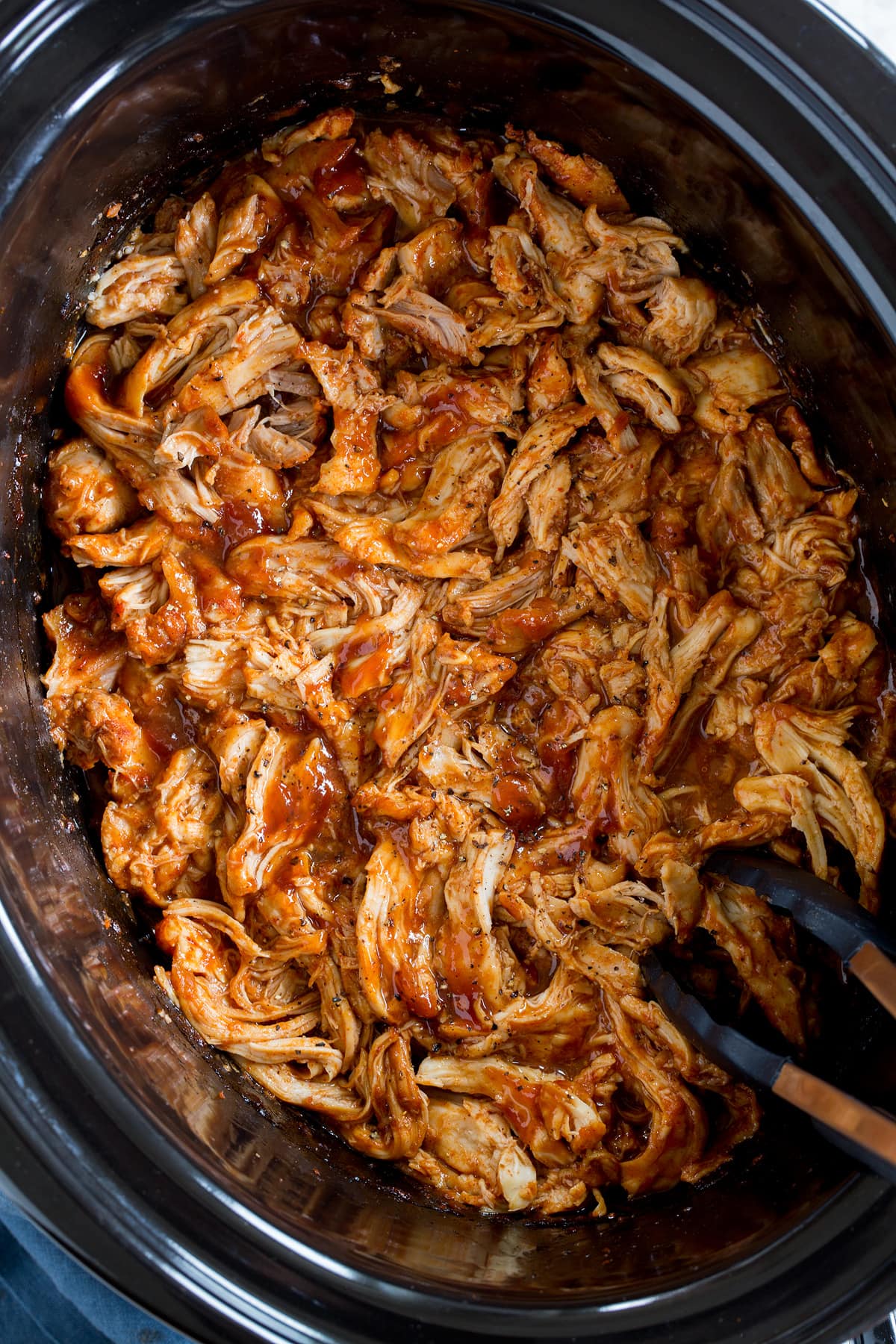 Photo: Slow cooker barbecue chicken in a black oval crockpot insert. Shown from overhead.