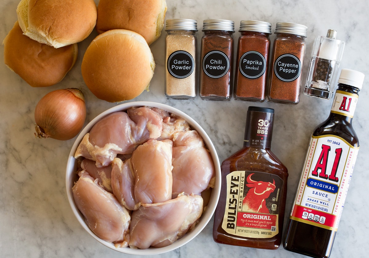 Photo: Ingredients used to make slow cooker barbecue chicken. Includes chicken thighs, bbq sauce, steak sauce, chili powder, smoked paprika, garlic powder, cayenne pepper, salt, pepper, buns, and yellow onion.
