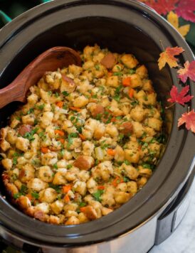Stuffing in a crockpot with decorative fall leaves and a green cloth to the side.