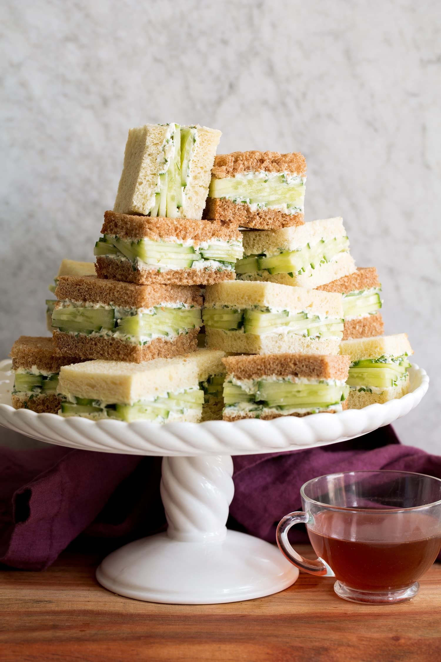 Cucumber sandwiches stacked on a white scalloped cake platter.