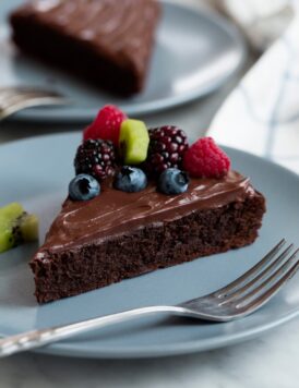 Flourless Chocolate Cake on a blue serving plate. Cake is topped with ganache and fresh fruit.