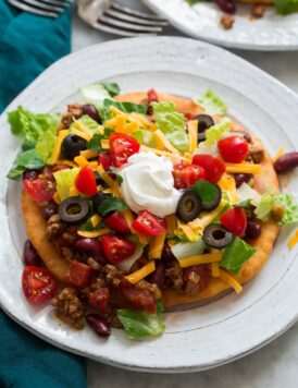 Homemade navajo taco on a plate. Made with homemade fry bread, ground beef and bean filling, lettuce, tomatoes, olives and sour cream.
