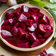 Chopped homemade pickled beets shown in a bowl surrounded by fresh beets.
