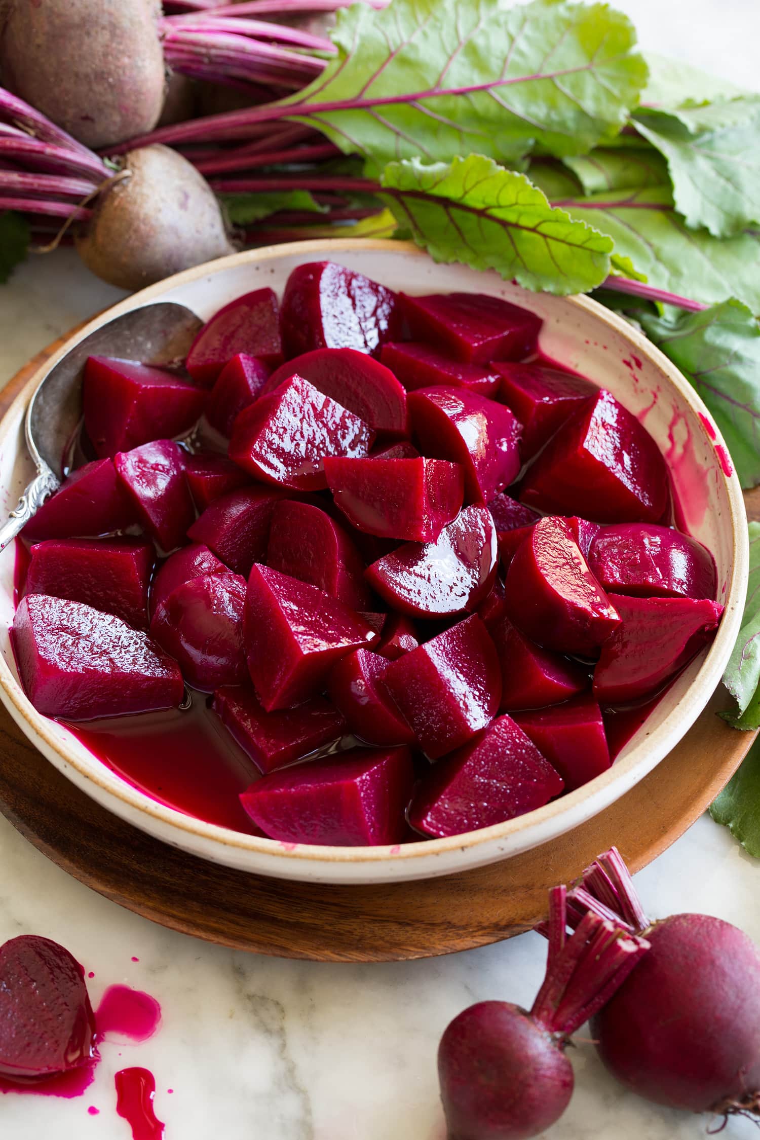 Chopped homemade pickled beets shown in a bowl surrounded by fresh beets.