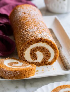 Pumpkin Roll on a white platter with a slice cut to show swirled cream cheese filling.