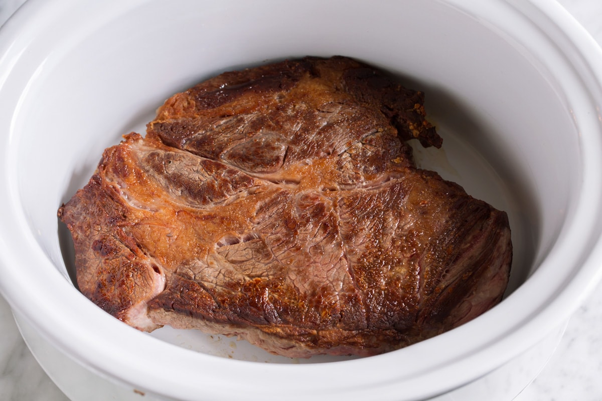 Showing how to make crockpot pot roast, placing seared chuck roast in a slow cooker.