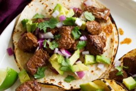 Single steak taco with avocado, cilantro and red onion shown close up.